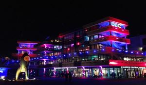 Ansicht des CCH bei Nacht. Fassade mit rotem und blauem Licht beleuchtet, davor steht eine Rakete.